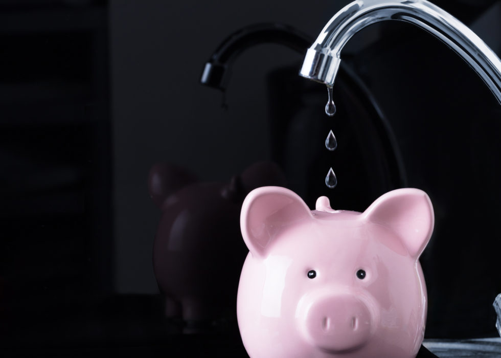 Chrome faucet dripping water above a pink piggy bank