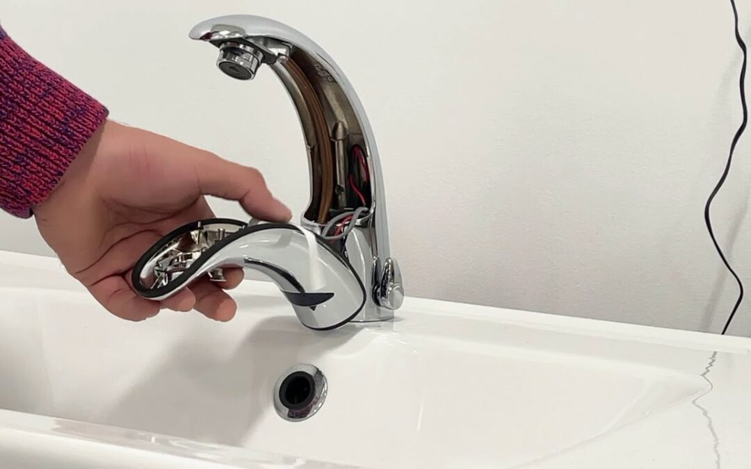 Hand holding the open cover of a chrome automatic faucet to reveal its wiring