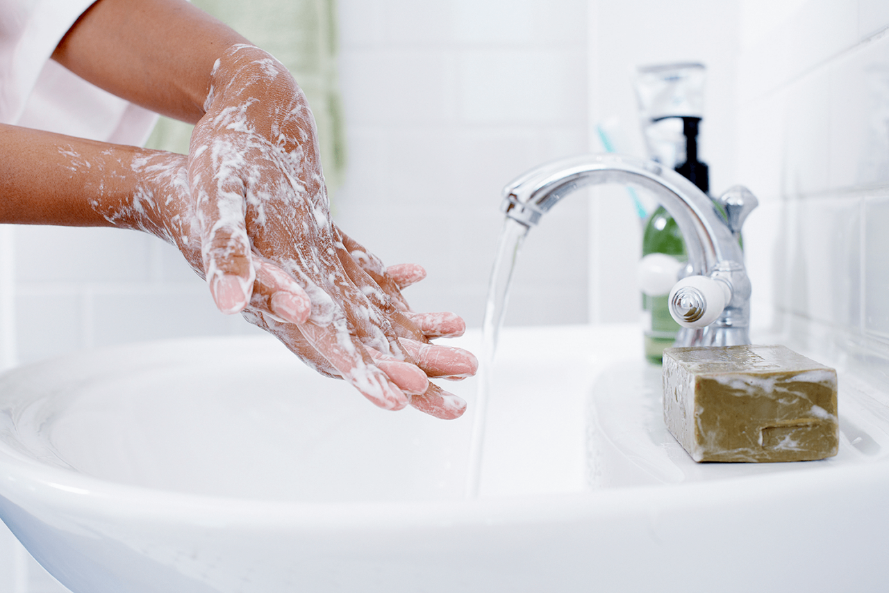 Hands being washed with soap beside a bathroom faucet