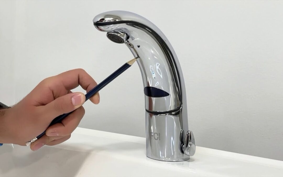 Hand holding a pencil near the sensor of a chrome FCI automatic faucet